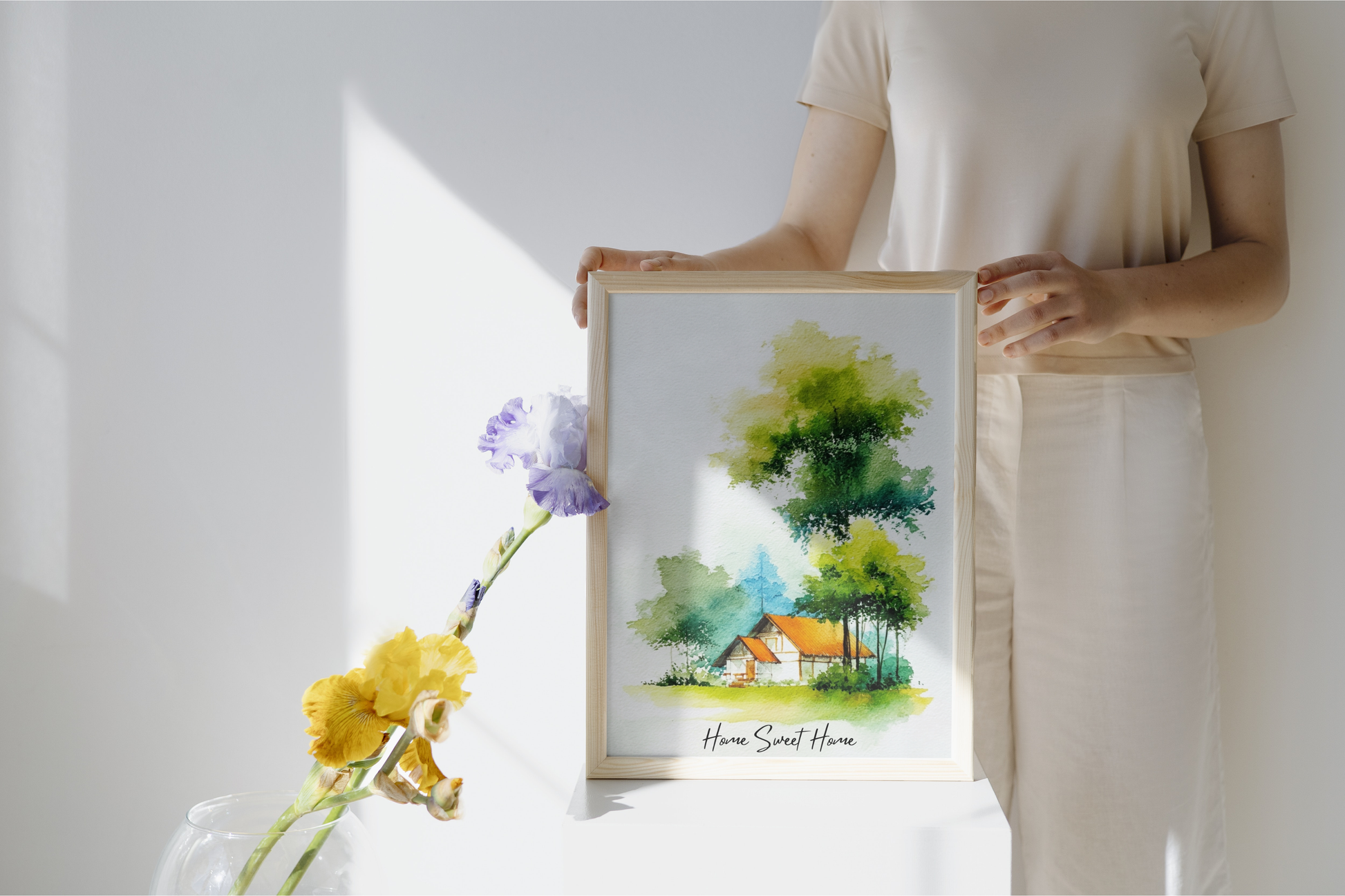 Person holding a framed watercolor painting of a house with trees and flowers.
